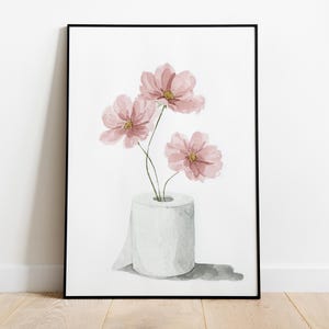 Puede incluir: Impresi&oacute;n art&iacute;stica en acuarela con flores rosas en un rollo de papel higi&eacute;nico. Las flores tienen centros amarillos y est&aacute;n sobre un fondo blanco. La obra de arte est&aacute; enmarcada en un marco negro.