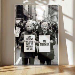 Könnte beinhalten: Schwarz-Weiß-Foto von zwei älteren Frauen, die bei einer Demonstration Schilder hochhalten. Auf einem Schild steht "I CAN'T BELIEVE WE STILL HAVE TO PROTEST THIS SHIT", auf dem anderen "ME NEITHER". Im Hintergrund eine Menschenmenge und Gebäude.