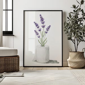 May include: A framed art print featuring a watercolor illustration of lavender sprigs emerging from a roll of toilet paper. The artwork has a white background and is framed in black. The image is displayed in a modern interior setting.