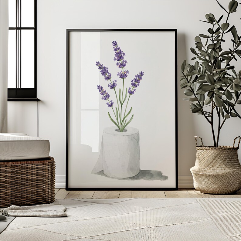 May include: A framed art print featuring a watercolor illustration of lavender sprigs emerging from a roll of toilet paper. The artwork has a white background and is framed in black. The image is displayed in a modern interior setting.