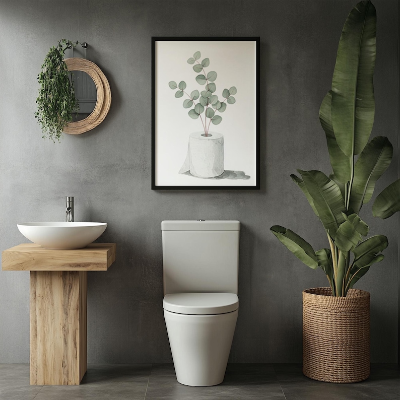 Op de afbeelding: Een moderne badkamer met een witte toilet, een houten wastafel met een witte wastafel en een ingelijste botanische print. Een grote plant in pot en een hangspiegel dragen bij aan de inrichting. De muren zijn neutraal grijs.