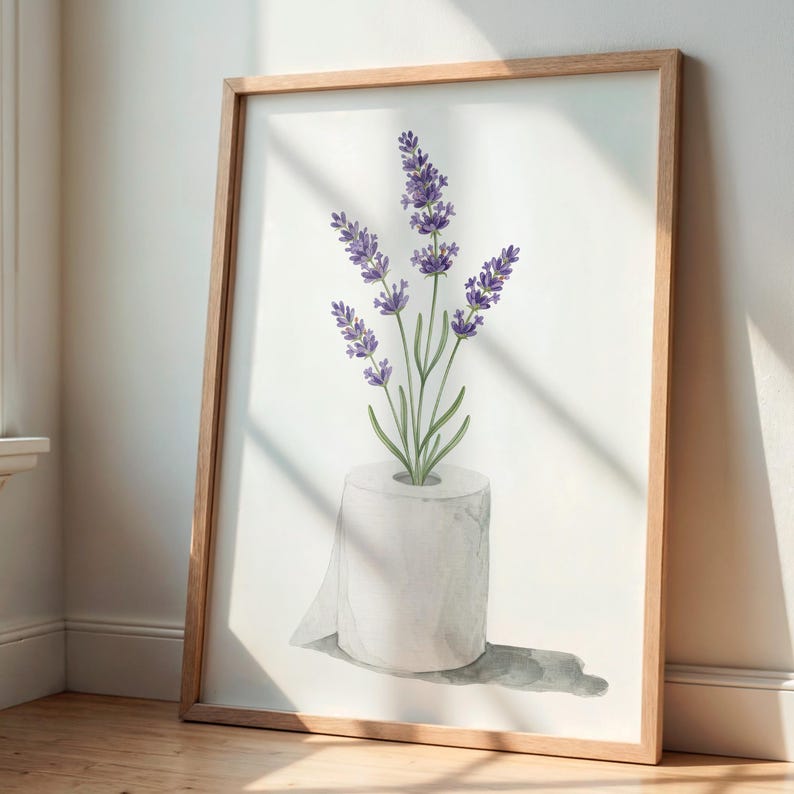 May include: A framed art print featuring a watercolor illustration of lavender flowers emerging from a roll of toilet paper. The lavender has purple blooms and green stems. The frame is made of light brown wood.