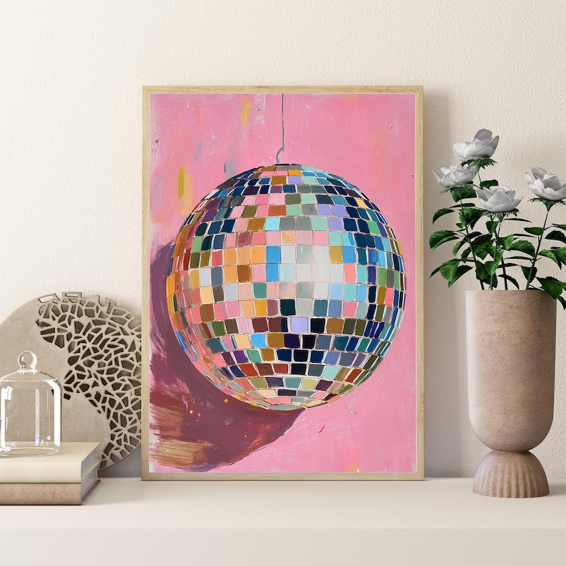 a vibrant, colorful disco ball with a pink background, hanging from the ceiling and casting a reflection on the wall below. The disco ball is surrounded by various decorative elements, including a vase with white flowers, a sculpture, and a stack of books.