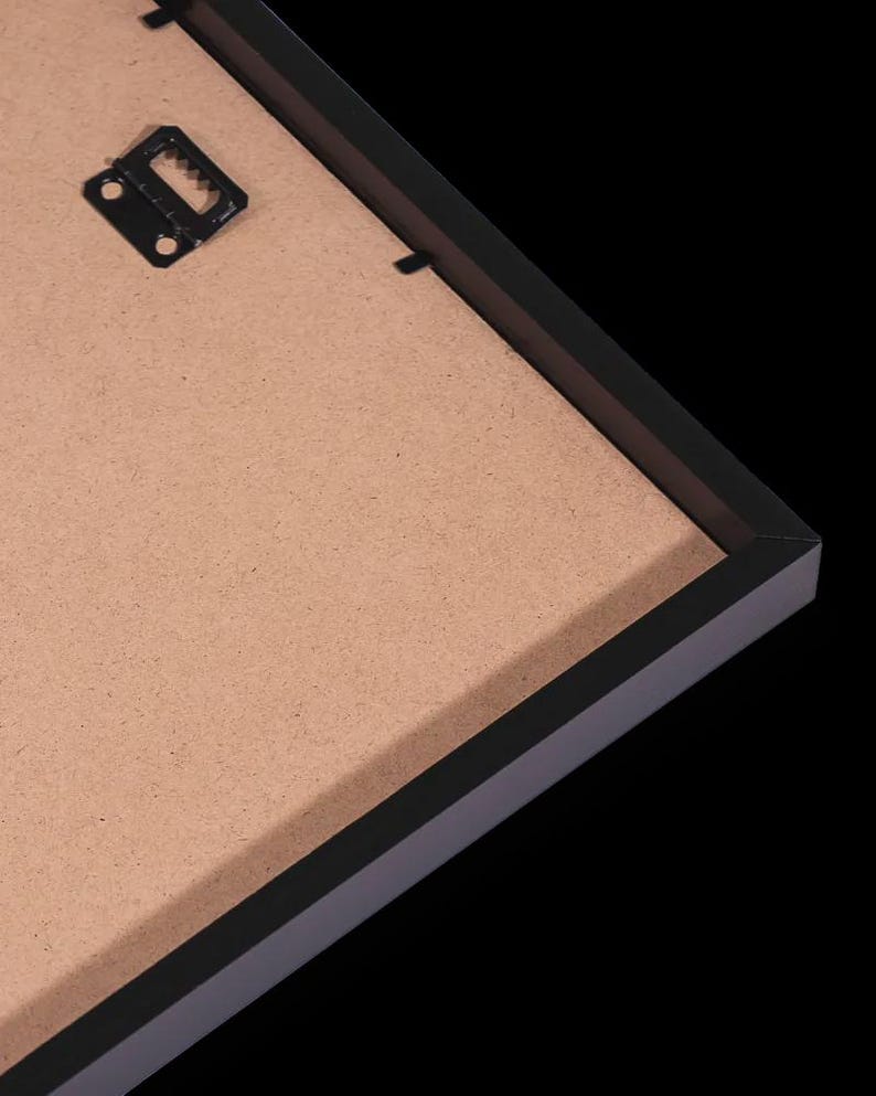 May include: A black picture frame with a brown backing. The frame has a simple, modern design with a black finish. A metal sawtooth hanger is attached to the back for wall mounting. The frame is set against a black background.