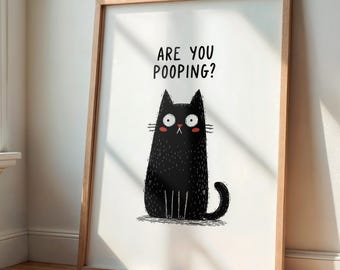 May include: A framed art print featuring a whimsical black cat illustration. The cat has wide eyes and rosy cheeks, with the text "ARE YOU POOPING?" above it. The artwork is set against a white background, framed in light wood.