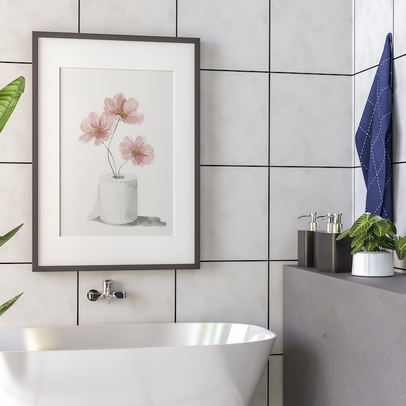 Puede incluir: Impresi&oacute;n art&iacute;stica enmarcada con flores rosas en un rollo de papel higi&eacute;nico. La obra de arte se exhibe en un ba&ntilde;o con azulejos blancos y una ba&ntilde;era moderna. Una toalla azul cuelga cerca.