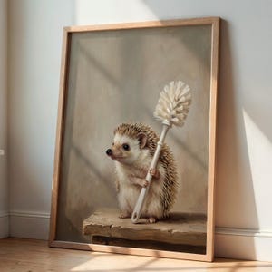 Könnte beinhalten: Ein gerahmter Kunstdruck, der einen braun-weißen Igel zeigt, der auf einer Holzoberfläche steht und eine weiße Toilettenbürste hält. Der Hintergrund ist in einem neutralen, gedämpften Beigeton gehalten, mit weichem Licht und Pinselstrukturen.