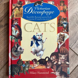 May include: A red book titled "Victorian Découpage Cats" featuring illustrations of various cats. The cover includes the text "Beautifully illustrated practical book containing 10 step-by-step projects" and the author's name, Hilary Hammond.