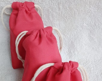 May include: Three red drawstring bags with white drawstrings. The bags are made of a soft, fabric material and are lined up in a row.