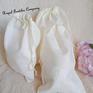 May include: Four white cotton drawstring bags on a white fluffy surface. The bags are made of natural fabric and have a simple design. The bags are ideal for storing small items or gifts.