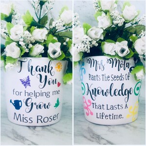 May include: Two white ceramic flower pots with floral arrangements. The pot on the left has the text "Thank You for helping me Grow Miss Roser". The pot on the right has the text "Mrs. Mola Plants The Seeds of Knowledge That Lasts A Lifetime."