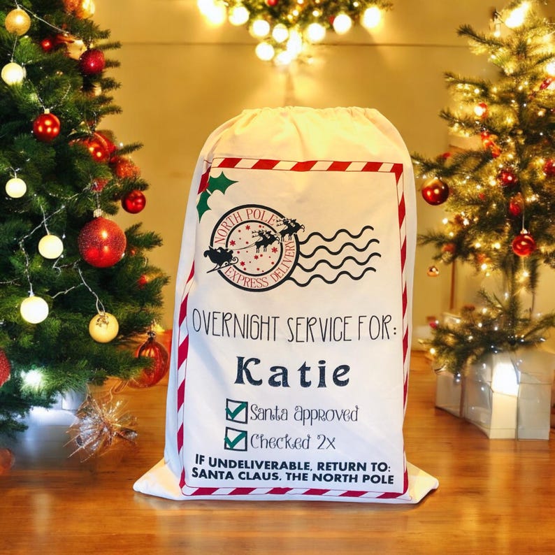 May include: White canvas Santa sack with red and white stripes. The sack has a black and white graphic of Santa's sleigh and the text "North Pole Express Delivery". The sack also has the text "Overnight Service For: Katie" and a checklist with the text "Santa Approved" and "Checked 2x". The bottom of the sack has the text "If undeliverable, return to: Santa Claus, The North Pole".