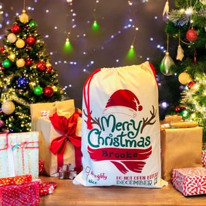 May include: A white canvas Santa sack with red drawstring and a green and red "Merry Christmas" graphic. The sack is personalized with the name "Brooke" and has a "Naughty or Nice" checkbox and the text "Do Not Open Before December 24th".