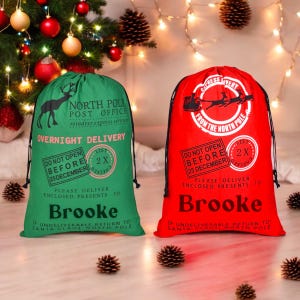 May include: Two red and green Christmas gift bags with white text and images. The bags are decorated with a reindeer, a sleigh, and a Santa Claus list. The text on the bags reads "North Pole Post Office" and "Express Delivery from the North Pole". The bags also have a "Do Not Open Before 25 December" stamp. The bags are personalized with the name "Brooke".