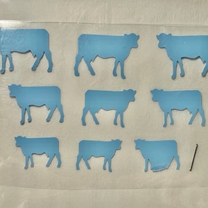 May include: Nine blue paper cow cutouts on a white background. The cows are all facing the same direction and are arranged in three rows of three.