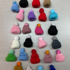 May include: Assortment of 25 colorful knitted hats with pom-poms. The hats are in various colors, including red, blue, green, pink, purple, black, white, and brown.
