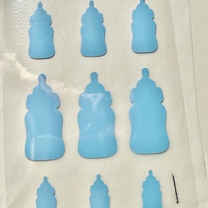 May include: Nine blue baby bottle shaped stickers on a clear sheet. The stickers are various sizes.