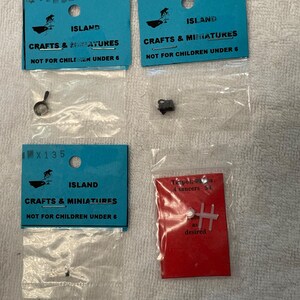 May include: Four small packages of miniature crafts and miniatures. The packages are labeled "Island Crafts & Miniatures" and "Not for Children Under 6". One package contains a small metal object, and another contains a red card with text.