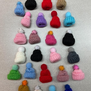 May include: A collection of 27 knitted hats with pom-poms in various colors, including red, blue, green, pink, purple, black, white, and brown.