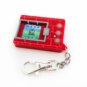 May include: Red and gray digital pet keychain with a pixelated image of a green creature on the screen. The keychain has a silver chain.