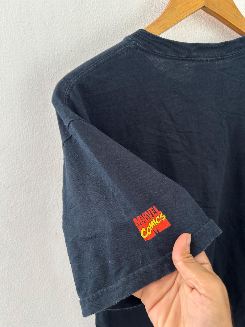 May include: Black t-shirt with the Marvel Comics logo in red and yellow on the sleeve. The shirt is made of a soft material and has a crew neck.