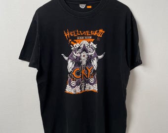 Könnte beinhalten: Schwarzes T-Shirt mit einem grafischen Design mit einem Schädel, Hörnern und dem Text "Hellview III" in Orange. Das Design enthält auch den Text "CRY" und die Daten "10.30.08 - 10.31.08". Das Shirt hängt an einem Holzbügel.