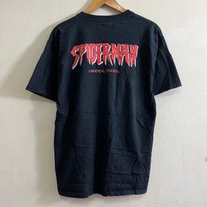 Op de afbeelding: Zwart T-shirt met een rode "Spider-Man" afbeelding en de tekst "Universal Studios" op de achterkant.