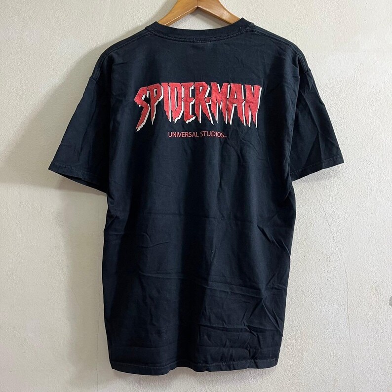 Op de afbeelding: Zwart T-shirt met een rode "Spider-Man" afbeelding en de tekst "Universal Studios" op de achterkant.