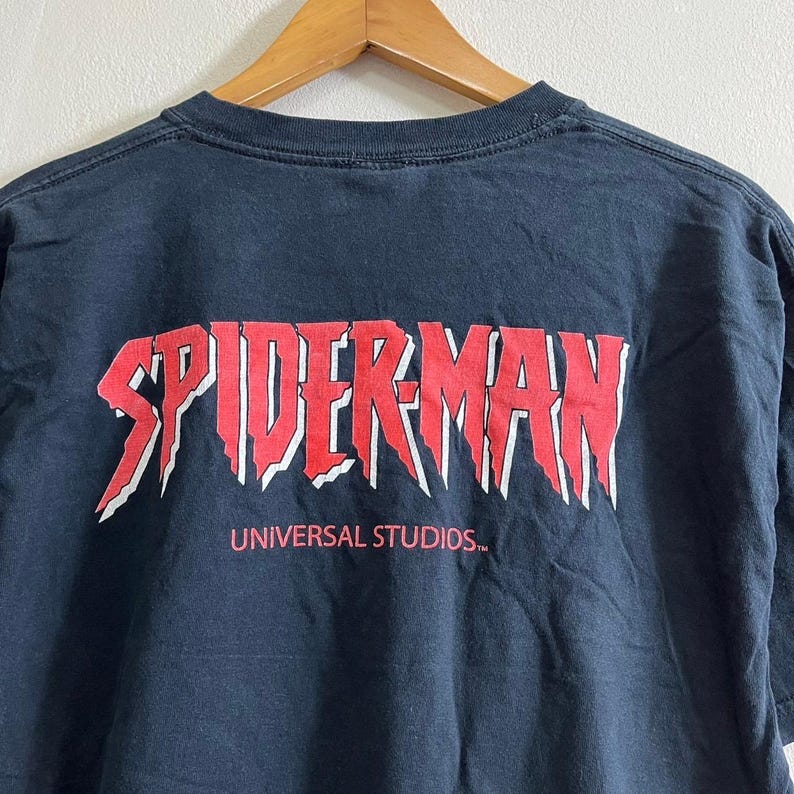 Op de afbeelding: Zwart T-shirt met een rode "Spider-Man" afbeelding en de tekst "Universal Studios" in wit.