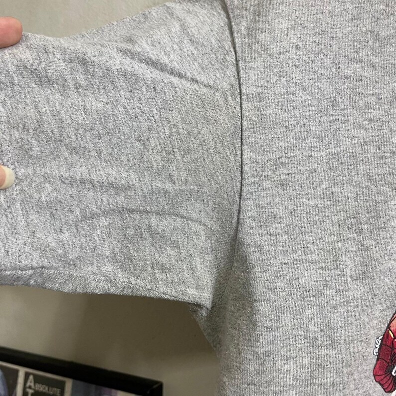 Puede incluir: Una camiseta gris con un estampado gr&aacute;fico descolorido de color rojo y negro. La camiseta est&aacute; hecha de un material suave y c&oacute;modo.