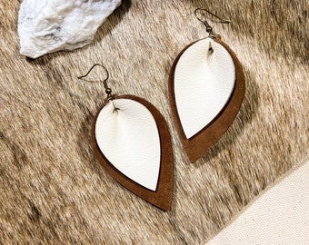 May include: A pair of brown and white leather earrings with a teardrop shape. The earrings are layered with a white leather piece on top of a brown leather piece.