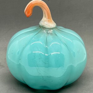May include: A teal blue glass pumpkin with a swirl design and an orange and white glass stem.