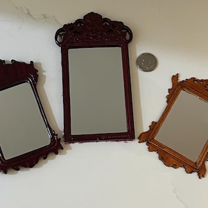 May include: Three rectangular mirrors with ornate, carved frames in varying shades of brown, ranging from dark mahogany to a lighter wood tone. A small silver-colored coin is positioned next to the central mirror for a sense of scale.