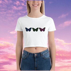 May include: White cropped t-shirt with three colorful butterfly designs. The butterflies are blue, green, and pink with black outlines.