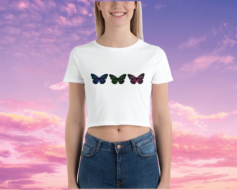 May include: White cropped t-shirt with three colorful butterfly designs. The butterflies are blue, green, and pink with black outlines.