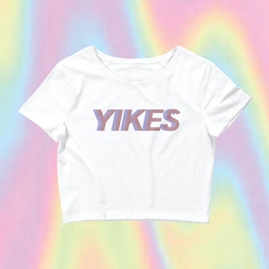 May include: White cropped t-shirt with the word "YIKES" printed in a purple and pink gradient.