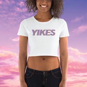 May include: White cropped t-shirt with the word "YIKES" printed in a purple and pink gradient.