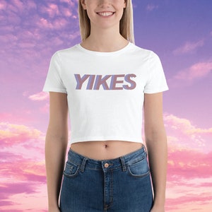 May include: White cropped t-shirt with the word "YIKES" printed in a purple and pink gradient.