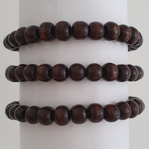 May include: Three brown wooden bead bracelets stacked on top of each other. The bracelets are made of round beads and are all the same size.