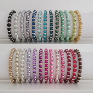 May include: A collection of 20 beaded bracelets in various colors, including black, white, gray, blue, green, pink, red, and brown. Each bracelet is made with small, round beads and silver accents.