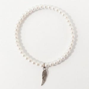 May include: A white pearl bracelet with a silver-colored wing charm. The bracelet is made of small, round, white pearls strung together. The wing charm is detailed and hangs from the center of the bracelet.