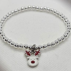 May include: A silver beaded bracelet with a reindeer charm. The charm has a white face, red nose, and red antlers. The bracelet is made of small, round, silver beads.