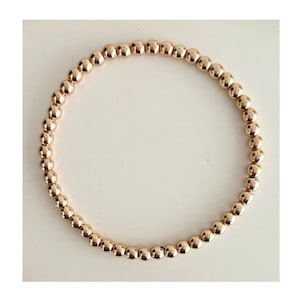 May include: A gold-toned beaded bracelet with small, round beads. The bracelet is made of metal and has a simple, elegant design.