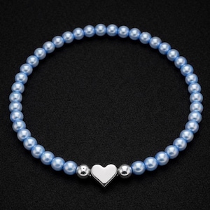 May include: Light blue beaded bracelet with a silver heart charm. The bracelet features small, round, light blue beads strung together, with a polished silver heart charm at the center. Two silver beads flank the heart. The bracelet is set against a black background.