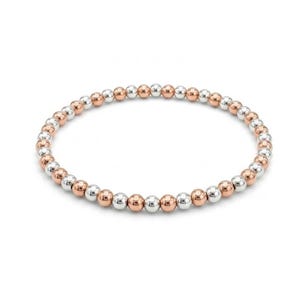May include: A circular stretch bracelet composed of alternating polished silver-tone and rose gold-tone spherical beads. The beads are uniform in size and arranged in a repeating pattern, creating a continuous metallic band with a reflective finish.