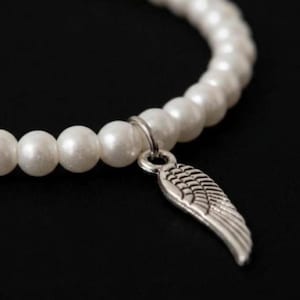 May include: A white pearl bracelet with a silver wing charm. The bracelet features a strand of round, lustrous white pearls. The silver charm is a detailed wing design, adding a touch of elegance to the jewelry.