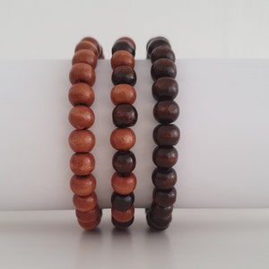 May include: Three wooden bead bracelets, one with brown beads, one with light brown beads, and one with a mix of brown and light brown beads.
