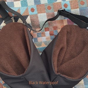 May include: A black waterproof bag with a brown fleece lining. The bag has a single adjustable strap and a metal ring.