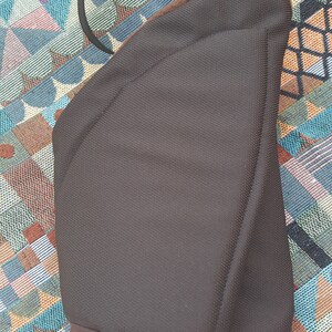 May include: A brown padded bag with a black adjustable strap. The bag has a curved shape and a soft, textured fabric.