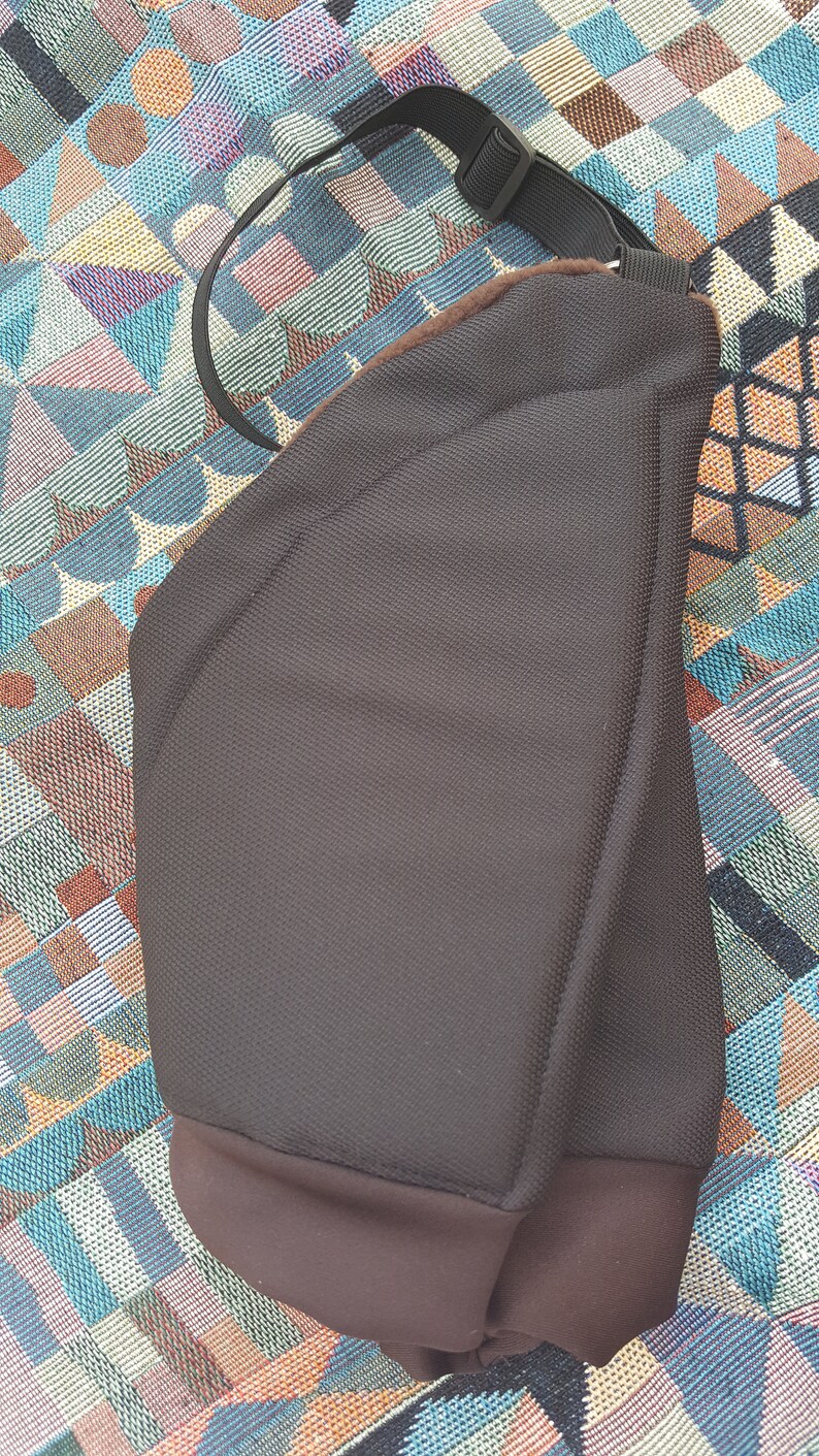 May include: A brown padded bag with a black adjustable strap. The bag has a curved shape and a soft, textured fabric.